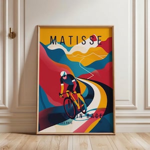 May include: A framed art print featuring a cyclist in a race, with the word "MATISSE" at the top. The artwork uses bold colors like red, yellow, and blue to depict a winding road and mountainous landscape. The text "IN RACE" and "DES ARTS" are also visible.