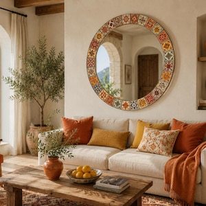 May include: A large round wall mirror featuring a decorative frame composed of colorful square tiles in shades of red, orange, yellow, and blue. The mirror reflects an interior space with arched doorways and a wooden door, mounted on a beige wall.