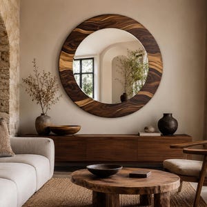 May include: A large circular wall mirror featuring a wide, thick frame crafted from dark brown wood with prominent, swirling natural grain patterns. The mirror surface is reflective and smooth, showcasing a clear view of an interior space.