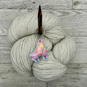 May include: A skein of cream colored yarn with a wooden knitting needle and a roller skate charm attached.