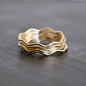 May include: A set of five gold and silver wavy rings stacked together. The rings are made of thin metal and have a simple, modern design.