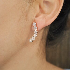 May include: A pair of gold-toned earrings with a curved design. The earrings are adorned with small, clear cubic zirconia stones.