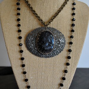 May include: A black cameo pendant necklace with a filigree design and a black beaded chain. The cameo features a woman's profile.