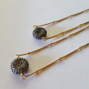 May include: Gold-toned necklaces with a delicate chain design. Each necklace features a small, round, textured pendant with a dark, sparkling surface. The necklaces are displayed on a white background.