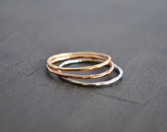 May include: Three thin, hammered metal rings stacked on top of each other. The rings are silver, rose gold, and gold.