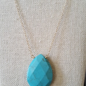 May include: A turquoise gemstone pendant necklace with a gold chain. The pendant is a teardrop shape with a faceted design.