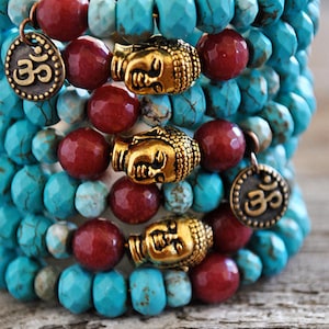 May include: A stack of turquoise and red beaded bracelets with gold Buddha head charms and Om symbols.