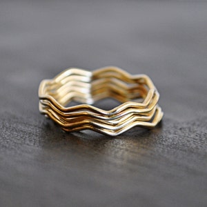 May include: A set of four gold and silver wavy rings stacked on top of each other. The rings are made of metal and have a smooth, polished finish.