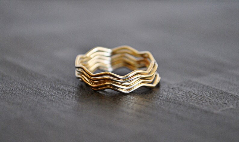May include: A set of four gold and silver wavy rings stacked on top of each other. The rings are made of metal and have a smooth, polished finish.