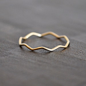 May include: A thin gold band ring with a wavy, zig-zag design.