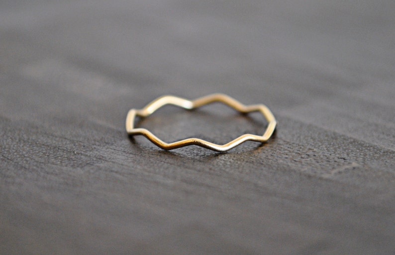 May include: A thin gold band ring with a wavy, zig-zag design.