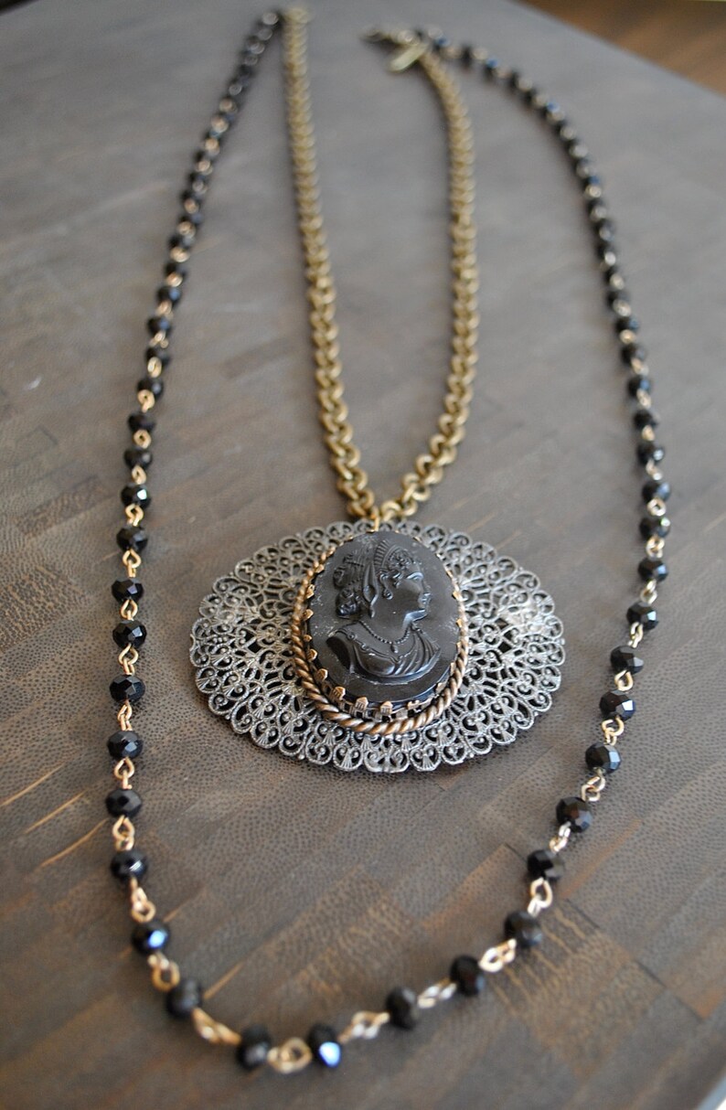 May include: A black cameo pendant necklace with a filigree design and a black beaded chain.