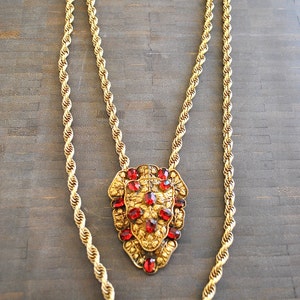 May include: Gold-tone necklace with a lion pendant. The pendant is adorned with red gemstones. The necklace has a rope chain design. A vintage-inspired jewelry piece.