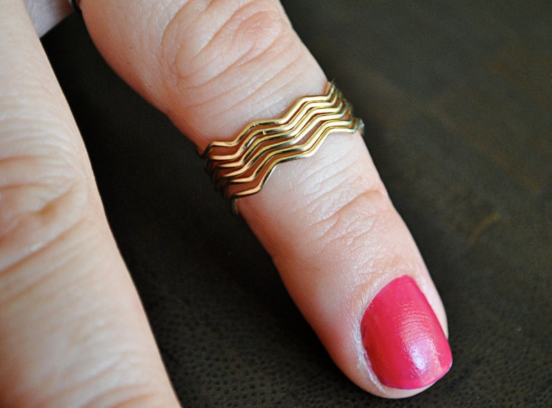 May include: A gold ring with a wavy design, worn on a finger with bright pink nail polish.