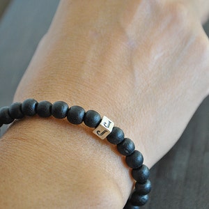 May include: A black beaded bracelet with a silver charm featuring the letter "J".