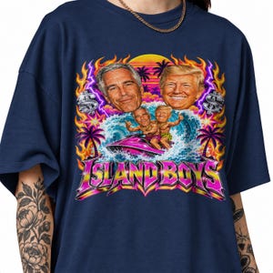 Peut inclure: Un t-shirt bleu marine avec une impression graphique représentant deux hommes sur un jet ski entourés de flammes, de palmiers et de signes dollar. Le texte "ISLAND BOYS" est imprimé en grandes lettres stylisées roses et jaunes en bas.