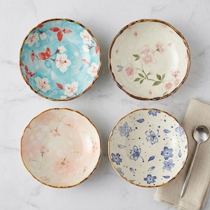 Puede incluir: Cuatro cuencos de cerámica con diseños florales. Cada cuenco tiene un patrón único: azul con flores blancas, blanco con flores rosas, rosa con flores y blanco con flores azules. Los cuencos tienen un borde ondulado y un borde marrón.