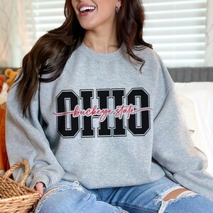 Digital design for crafting svg file for cricut silhouette print and cut clip art iron on transfer. Ohio is in an all capital double lined collegiate font. Sliced through the center in a red long tail cursive font it says buckeye state.