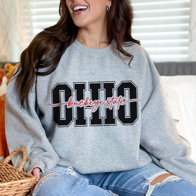 Digital design for crafting svg file for cricut silhouette print and cut clip art iron on transfer. Ohio is in an all capital double lined collegiate font. Sliced through the center in a red long tail cursive font it says buckeye state.