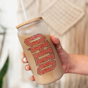 Puede incluir: Un vaso de vidrio esmerilado con tapa de madera y pajita. La palabra "OHIO" est&aacute; impresa en un dise&ntilde;o de estampado de leopardo rojo y gris. El vaso est&aacute; lleno de un l&iacute;quido marr&oacute;n claro.