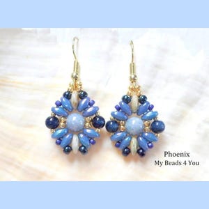 May include: A pair of dangle earrings featuring a central light blue round bead surrounded by a geometric pattern of dark blue, light blue, and metallic gold seed beads and oval-shaped beads, suspended from gold-toned metal earring hooks.