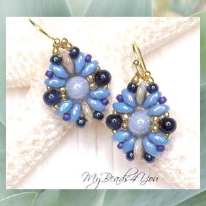 May include: A pair of dangle earrings featuring a central light blue round bead surrounded by a floral pattern of blue petal-shaped beads, dark navy round beads, and small gold-tone seed beads. The earrings hang from gold-tone metal hooks.