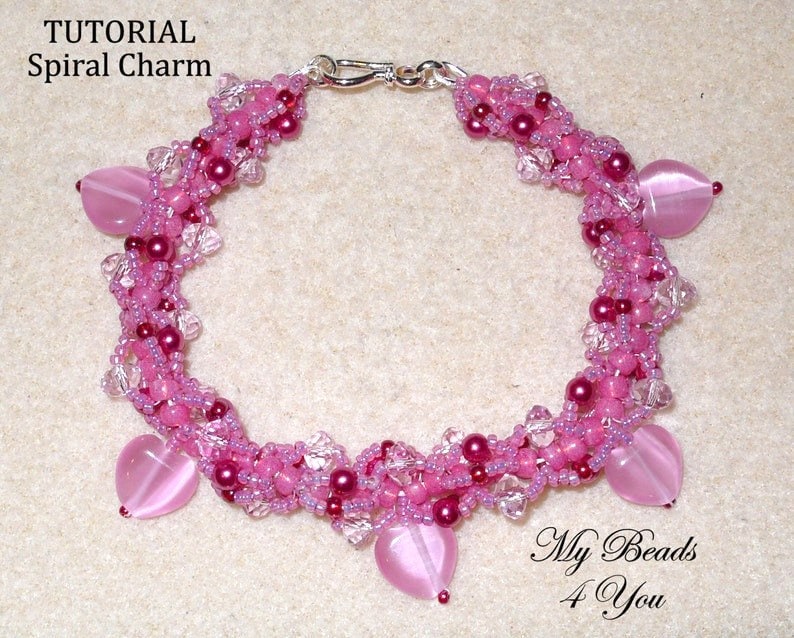 Op de afbeelding: Een handgemaakte roze kralenarmband met hartvormige bedels. De armband heeft een spiraalvormig ontwerp met verschillende roze tinten en heldere kristallen accenten. De tekst "TUTORIAL Spiral Charm" is zichtbaar.