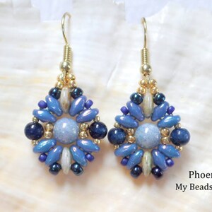 May include: A pair of dangle earrings featuring a central light blue round bead surrounded by a geometric pattern of dark blue, light blue, and metallic gold seed beads. The earrings hang from gold-toned hooks. Text reads: Phoenix My Beads 4 You.