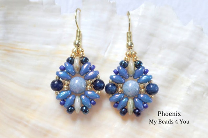 May include: A pair of dangle earrings featuring a central light blue round bead surrounded by a geometric pattern of dark blue, light blue, and metallic gold seed beads. The earrings hang from gold-toned hooks. Text reads: Phoenix My Beads 4 You.