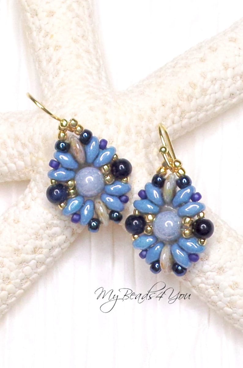 May include: A pair of drop earrings featuring a central light blue round bead surrounded by a floral pattern of elongated light blue, dark blue, and purple beads, accented with small gold metallic beads and gold-toned ear wires.