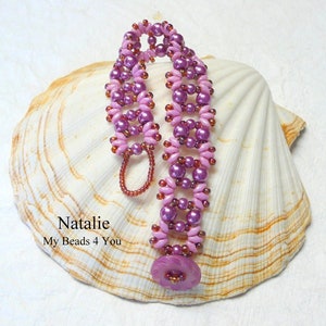 K&ouml;nnte beinhalten: Ein rosa und violettes Perlenarmband mit Blumenmuster. Das Armband liegt auf einem wei&szlig;en Muschelhintergrund. Der Text "Natalie My Beads 4 You" ist unterhalb des Armbands sichtbar.