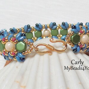 May include: A beaded bracelet with a floral design. The bracelet features blue, green, pink, and gold beads. The clasp is gold-colored. The bracelet is approximately 7 inches (17.78 cm) in length. The text "Carly MyBeads4You" is visible.