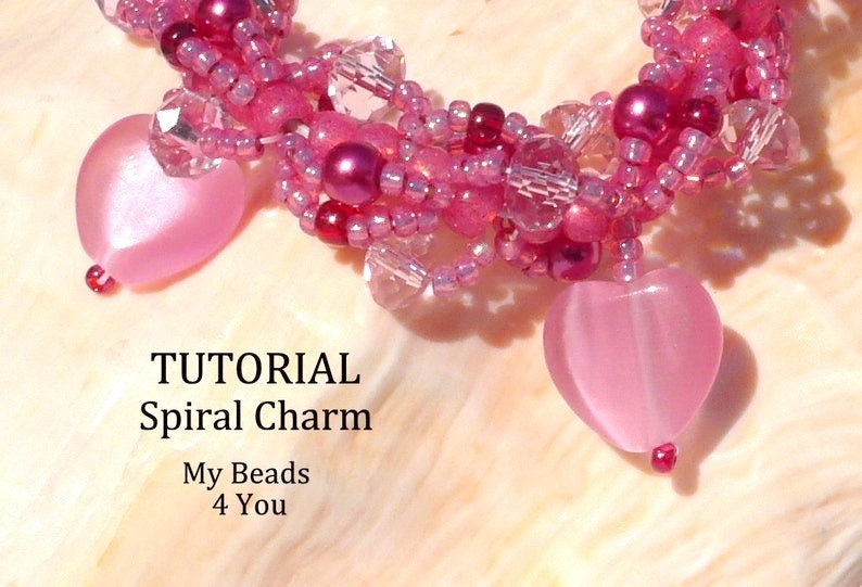 Op de afbeelding: Een close-up van een spiraalvormige bedeltutorial. De bedel is gemaakt van roze kralen en heeft twee hartvormige hangers. De tekst "TUTORIAL Spiral Charm My Beads 4 You" is zichtbaar.
