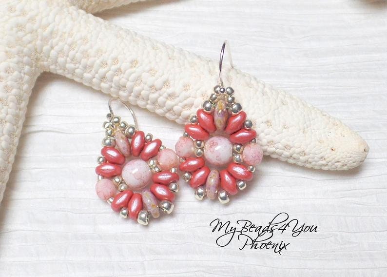 May include: A pair of teardrop-shaped earrings featuring a central round pink marbled bead surrounded by a ring of metallic silver seed beads and elongated coral-colored petal beads. The earrings hang from silver-toned hooks. Text reads My Beads4You Phoenix.