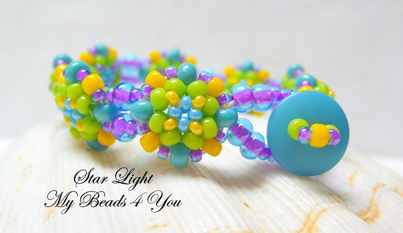 Peut inclure: Un bracelet en perles avec une fermeture bouton turquoise. Le bracelet est fait de petites perles color&eacute;es dans des tons de jaune, vert, bleu et violet. Les perles sont dispos&eacute;es en forme de fleur. Le bracelet est sur un fond blanc.