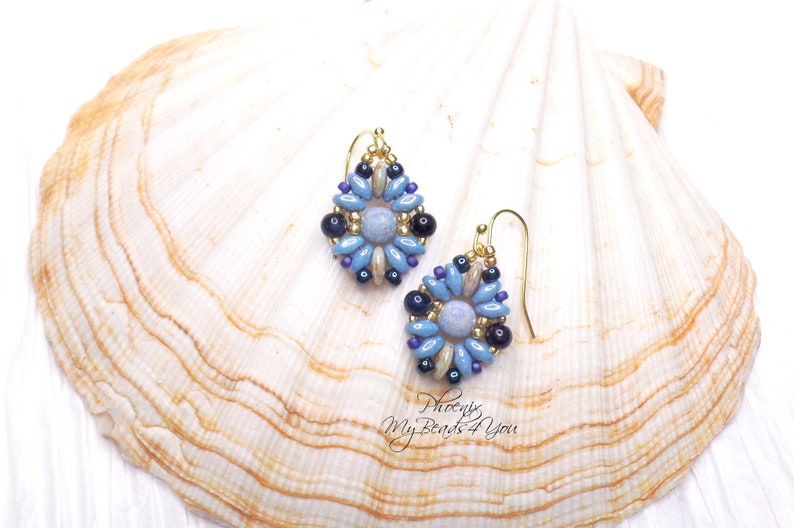 May include: A pair of drop earrings featuring a central light blue bead surrounded by a floral pattern of blue, dark blue, and metallic gold seed beads. The earrings are suspended from gold-toned metal hooks and include the text Phoenix MyBeads4You.