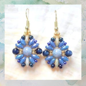 May include: A pair of dangle earrings featuring a central light blue round bead surrounded by a geometric pattern of smaller blue, dark blue, and metallic gold beads. The earrings are suspended from gold-toned metal hooks for pierced ears.
