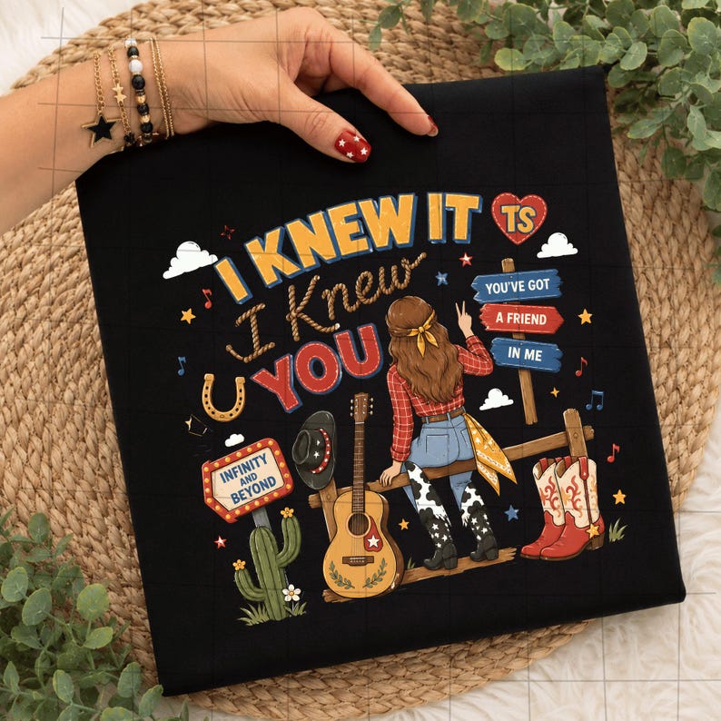 K&ouml;nnte beinhalten: Ein schwarzes T-Shirt mit einem Grafikdruck mit dem Text I KNEW IT I KNEW YOU, INFINITY AND BEYOND und YOU'VE GOT A FRIEND IN ME. Das Design zeigt eine Person mit langem braunem Haar, eine Gitarre, einen Kaktus und Cowboystiefel.