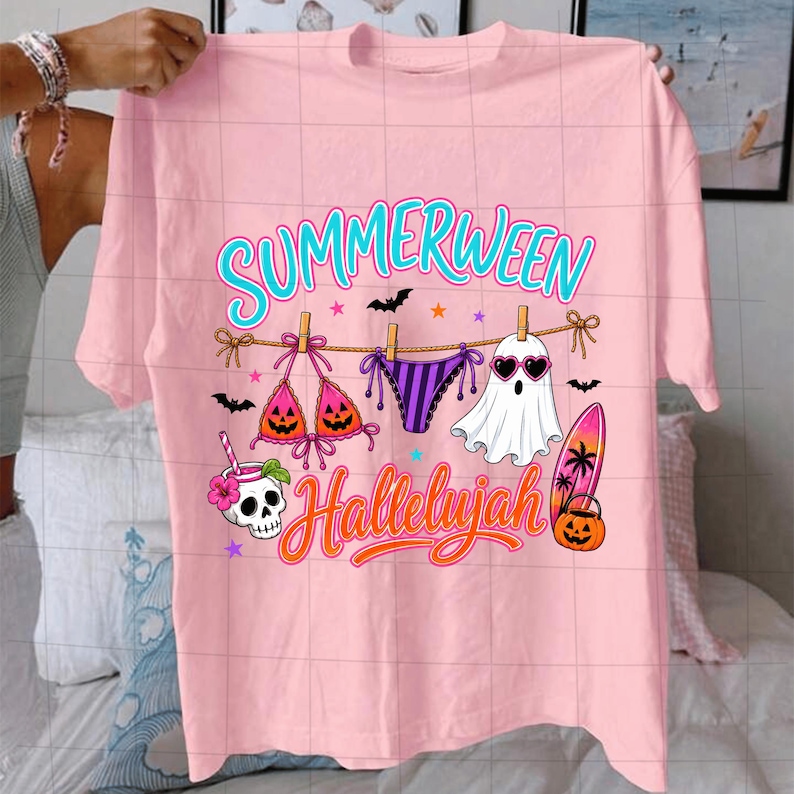 Puede incluir: Una camiseta rosa claro con un gr&aacute;fico que incluye el texto "SUMMERWEEN" y "Hallelujah". El dise&ntilde;o muestra un tendedero con un top de bikini, una braga de bikini y un fantasma con gafas de sol de coraz&oacute;n, adem&aacute;s de una calavera, una tabla y una calabaza.