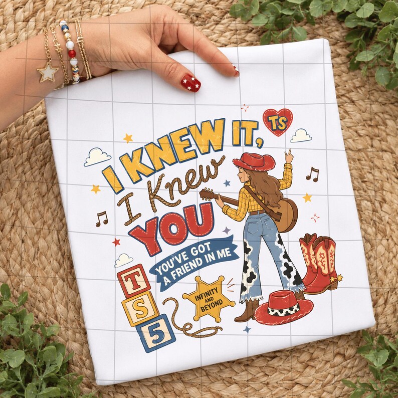 K&ouml;nnte beinhalten: Ein wei&szlig;es T-Shirt mit einer bunten Grafik und dem Text I KNEW IT, I KNEW YOU, YOU'VE GOT A FRIEND IN ME, TS 5 sowie INFINITY AND BEYOND. Das Design zeigt eine Cowgirl mit Gitarre, Cowboystiefel, einen Hut und verschiedene Sternsymbole.