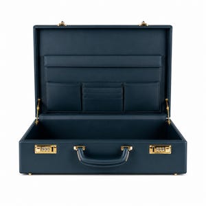 Pode incluir: Maleta de couro azul marinho aberta com ferragens douradas. O interior apresenta vários bolsos e compartimentos para organização. A maleta tem uma alça e fechaduras de combinação. Um acessório clássico e profissional.