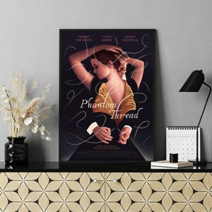 Può includere: Un poster incorniciato del film "Il filo nascosto" con Daniel Day-Lewis, Vicky Krieps e Lesley Manville. Il poster ha uno sfondo scuro con una donna in abito dorato e il titolo del film in scrittura bianca.