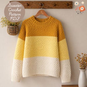 May include: A handmade, color-blocked sweater in shades of mustard yellow, light yellow, and cream. The sweater is hanging on a wooden hanger against a neutral wall. The text "Sweater Crochet Pattern PDF" is in a circle in the upper left.