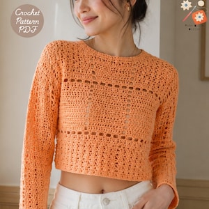 May include: A long-sleeved, orange crochet jumper featuring a round neckline and a textured, open-work stitch pattern. The garment is cropped at the waist. Text in the image reads: Crochet Pattern PDF and YARN BLOOM DESIGN.