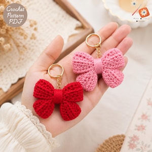 May include: Two crochet bow keychains, one in bright red and one in soft pink, each featuring a gold-toned metal keyring and chain. The text Crochet Pattern PDF is visible in the upper left corner, and Yarn Bloom Design is in the upper right.