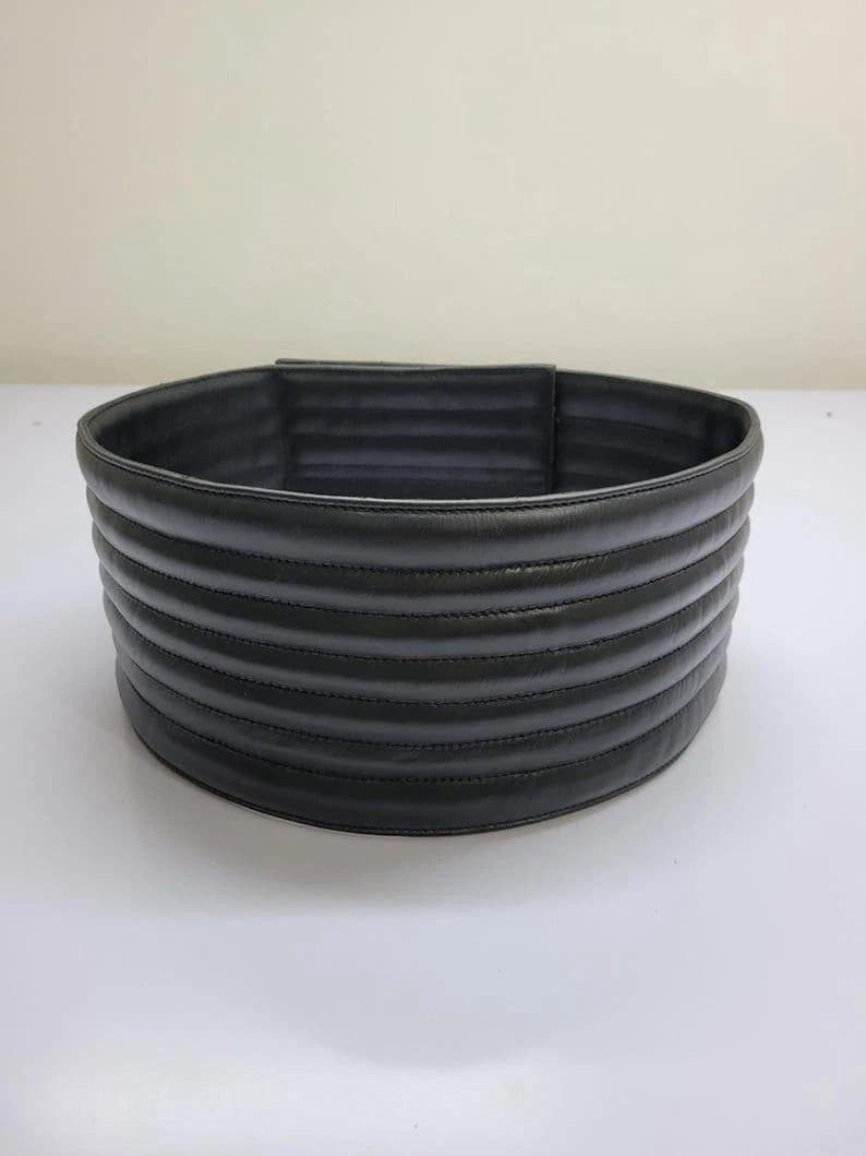 Puede incluir: Un cintur&oacute;n ancho de color negro que presenta una serie de canales horizontales acolchados y acolchados a lo largo de toda su longitud. El cintur&oacute;n tiene un acabado mate liso y una forma cil&iacute;ndrica estructurada con costuras visibles.