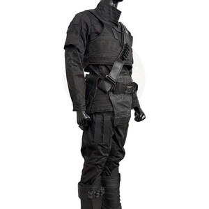 May include: A black tactical outfit consisting of a long-sleeved shirt with reinforced stitching, a structured chest plate, and matching trousers. The ensemble includes a utility belt, a diagonal shoulder strap with loops, and tall boots.
