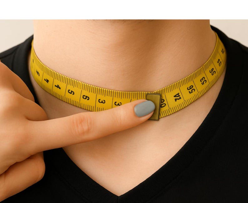 May include: A yellow flexible measuring tape wrapped around a neck, showing black numerical markings in centimeters. The tape is secured with a small rectangular metal clasp, indicating a measurement of approximately 60 centimeters in total length.
