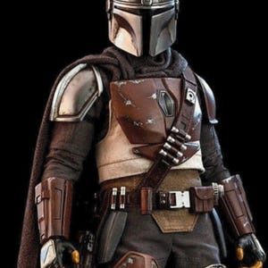 May include: A detailed action figure of a Mandalorian warrior, featuring a silver helmet, brown and tan armor, and a dark cape. The figure has a utility belt with pouches and a blaster holster. The overall design is intricate and realistic, set against a black background.