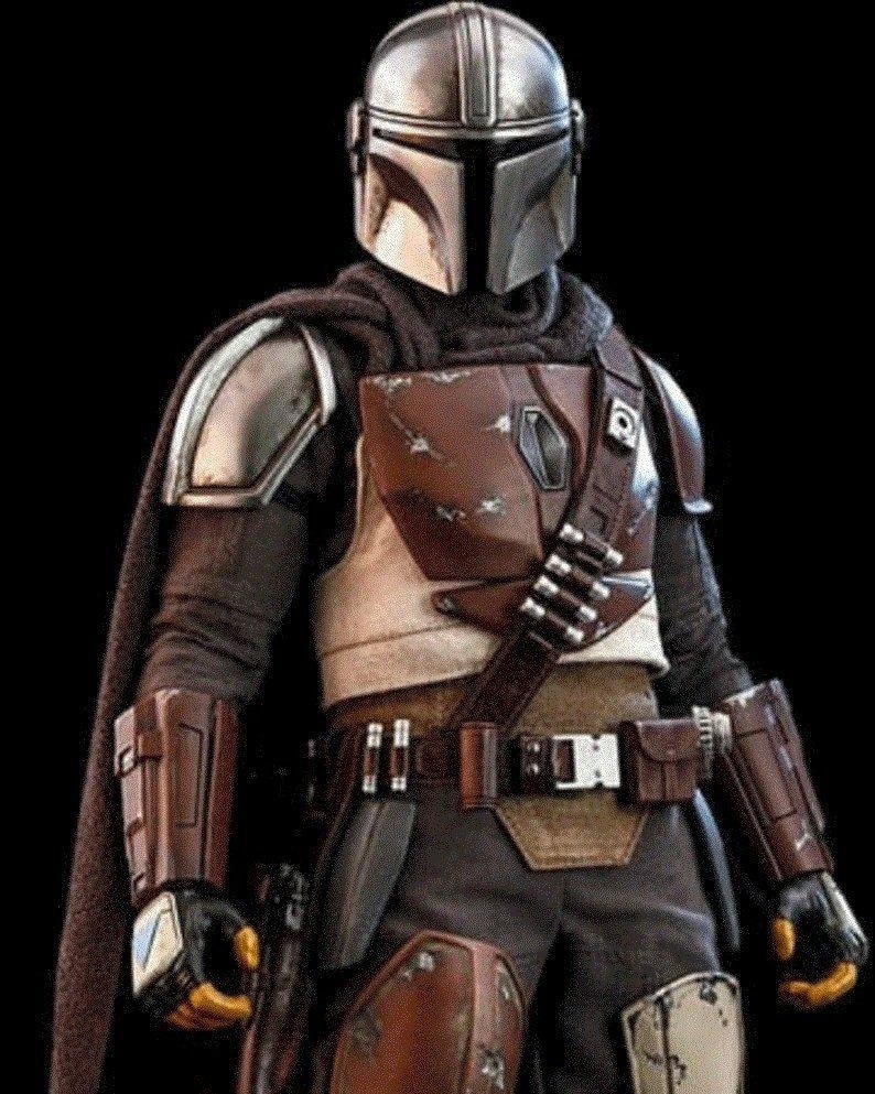 May include: A detailed action figure of a Mandalorian warrior, featuring a silver helmet, brown and tan armor, and a dark cape. The figure has a utility belt with pouches and a blaster holster. The overall design is intricate and realistic, set against a black background.
